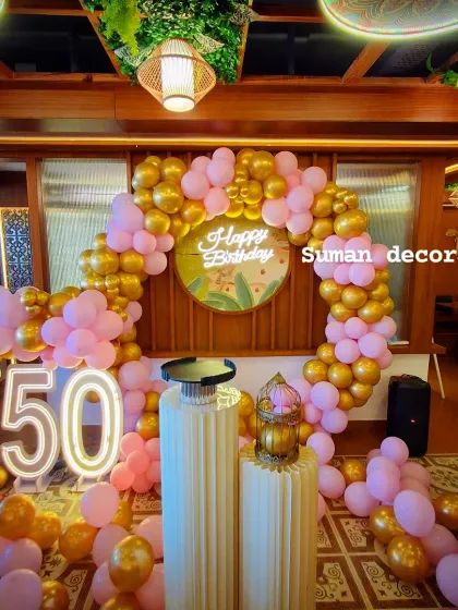 An elegant 50th birthday party decor in a pink and gold color scheme. This setup includes a large circular balloon arch, a custom "Happy Birthday" backdrop, and large light-up marquee numbers to mark the special milestone.