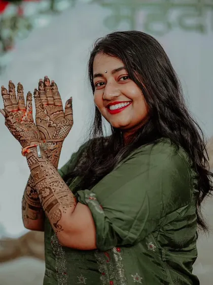 A radiant bride with a beautiful smile, proudly displaying her full bridal mehendi. The dark stain looks incredible.