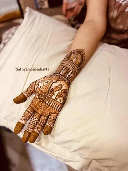 A close-up of a traditional bridal design on a single hand. This piece features a beautiful peacock and architectural elements, showcasing the fine line work.