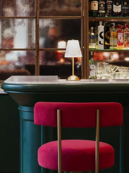 Detail is everything in creating ambiance. In this club bar, the contrast between the plush red velvet of the stool, the deep green paneling, and the warm glow from a classic table lamp creates a composition that feels both sophisticated and inviting.