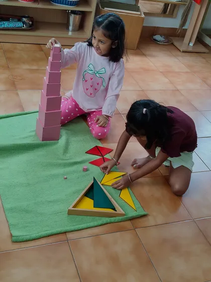 Here, two children collaborate on sensorial materials, the iconic Pink Tower and geometric puzzles. This moment captures the beauty of our mixed-age community, where older children guide younger ones, and everyone learns the value of teamwork and shared discovery.