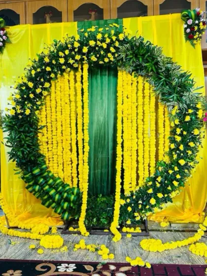 A bright and cheerful Haldi ceremony backdrop. The large circular arch is made entirely of fresh marigolds and green leaves, set against vibrant yellow drapes to bring energy and joy to the celebration.
