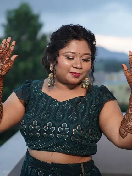 A lovely bride showing her hands, adorned with portrait mehendi, against the backdrop of a beautiful evening sky.