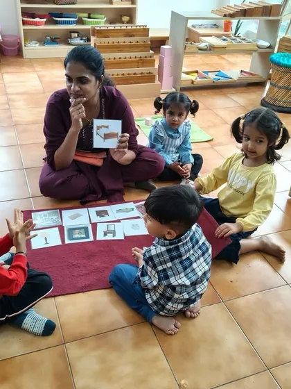 A teacher's role in a Montessori classroom is to be a guide, not a lecturer. This image shows a gentle, interactive group lesson with classified picture cards, which helps build vocabulary and encourages conversation among peers in a supportive setting.