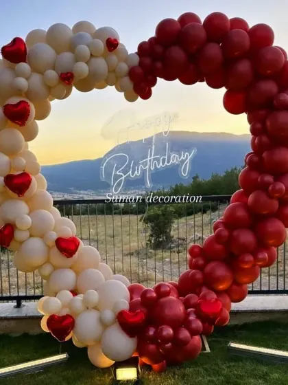 A beautiful heart-shaped balloon arch against a scenic outdoor background. This romantic setup combines red and white balloons with a "Happy Birthday" neon sign, making it a perfect photo backdrop for anniversaries or birthdays.
