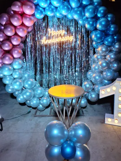 Anniversaries are so special, and I aim to create a truly romantic atmosphere. This first-anniversary setup features a stunning balloon ring with chrome balloons, a shimmering backdrop, and a neon sign, creating the perfect intimate corner for a couple to celebrate their journey.