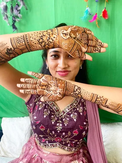 A beautiful bride framing her face with her hands, showing off a detailed design that includes elephants and other traditional patterns.