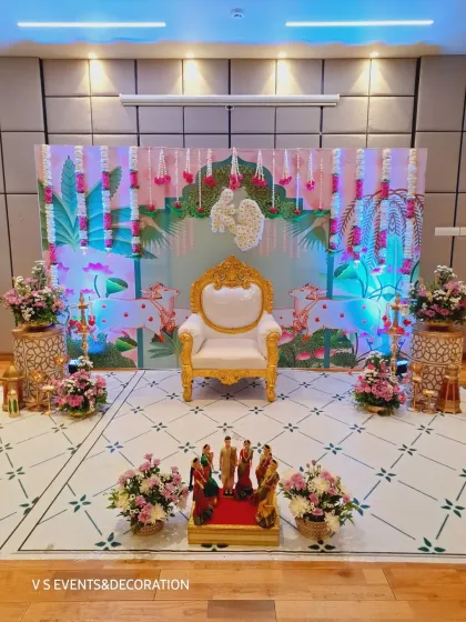 A complete stage setup for a Sreemantham, blending modern aesthetics with traditional touches. The elegant throne for the mother-to-be is the centerpiece, framed by a custom-printed backdrop, fresh flower garlands, and warm lighting to create a perfect photo opportunity.