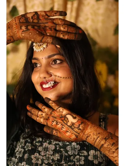 The bride frames her smiling face with her beautifully decorated hands, showing off the detailed peacock and floral designs.