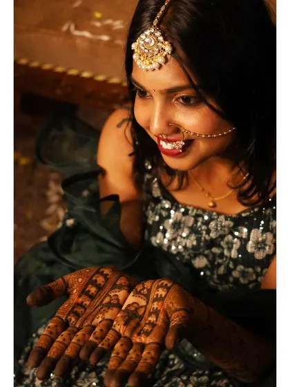 A happy bride with a beautiful nose ring and maang tikka, her hands adorned with dark, intricate mehendi. Her joyful expression is the best compliment.