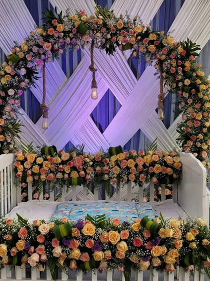 This is a more modern take on a cradle ceremony decoration, using a full arch of pastel roses and baby's breath. The hanging Edison bulbs add a warm, rustic touch to the elegant floral design.