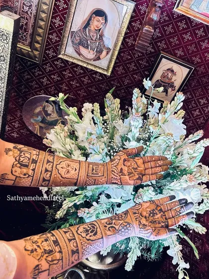 A bride's hands, adorned with intricate mehendi, held over a bouquet of white flowers. The design features symbolic figures and patterns, creating an artistic and traditional look.