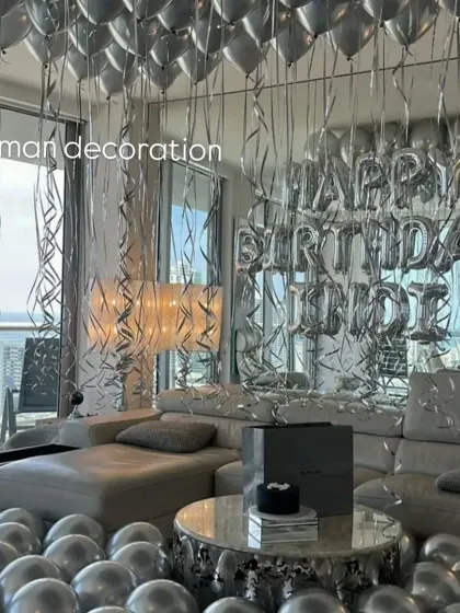 I can fill a whole room with balloons for a big surprise. This birthday setup features hundreds of silver helium balloons covering the ceiling and floor, with a 'Happy Birthday' foil balloon banner against a tinsel curtain backdrop.