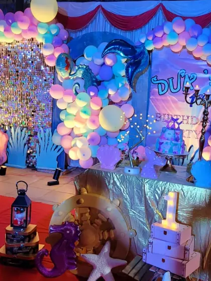 I dive deep into details for themes like this underwater mermaid party. The setup includes a beautiful shimmer wall, iridescent balloon garlands, and custom props like coral cutouts, seahorses, and a mermaid-themed cake table to create an enchanting ocean world.