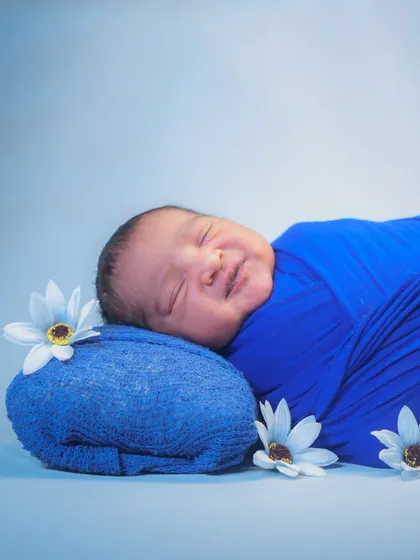 Sometimes, the simplest shots are the most beautiful. This little one's dreamy smile, swaddled snugly in a soft blue wrap, shows the pure, peaceful nature of a newborn.